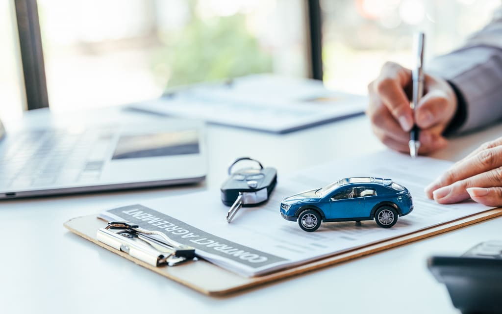 An automotive specialist signing vehicle paperwork beside a calculator and car keys
