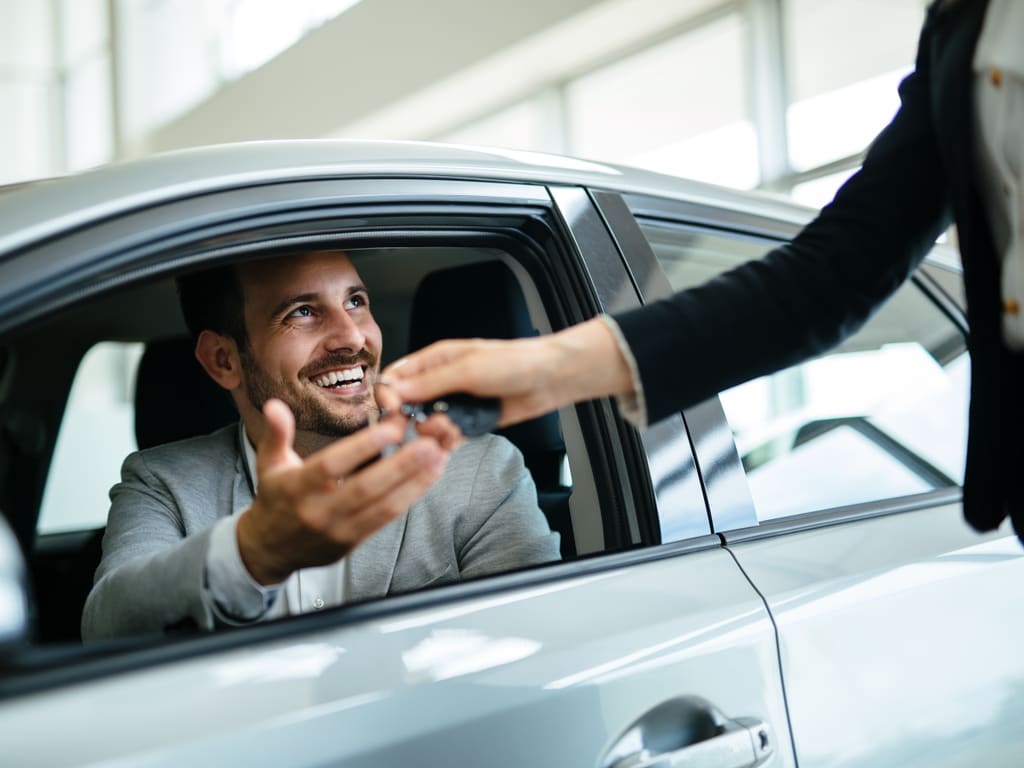 A happy driver receiving car keys from a salesperson at a dealership